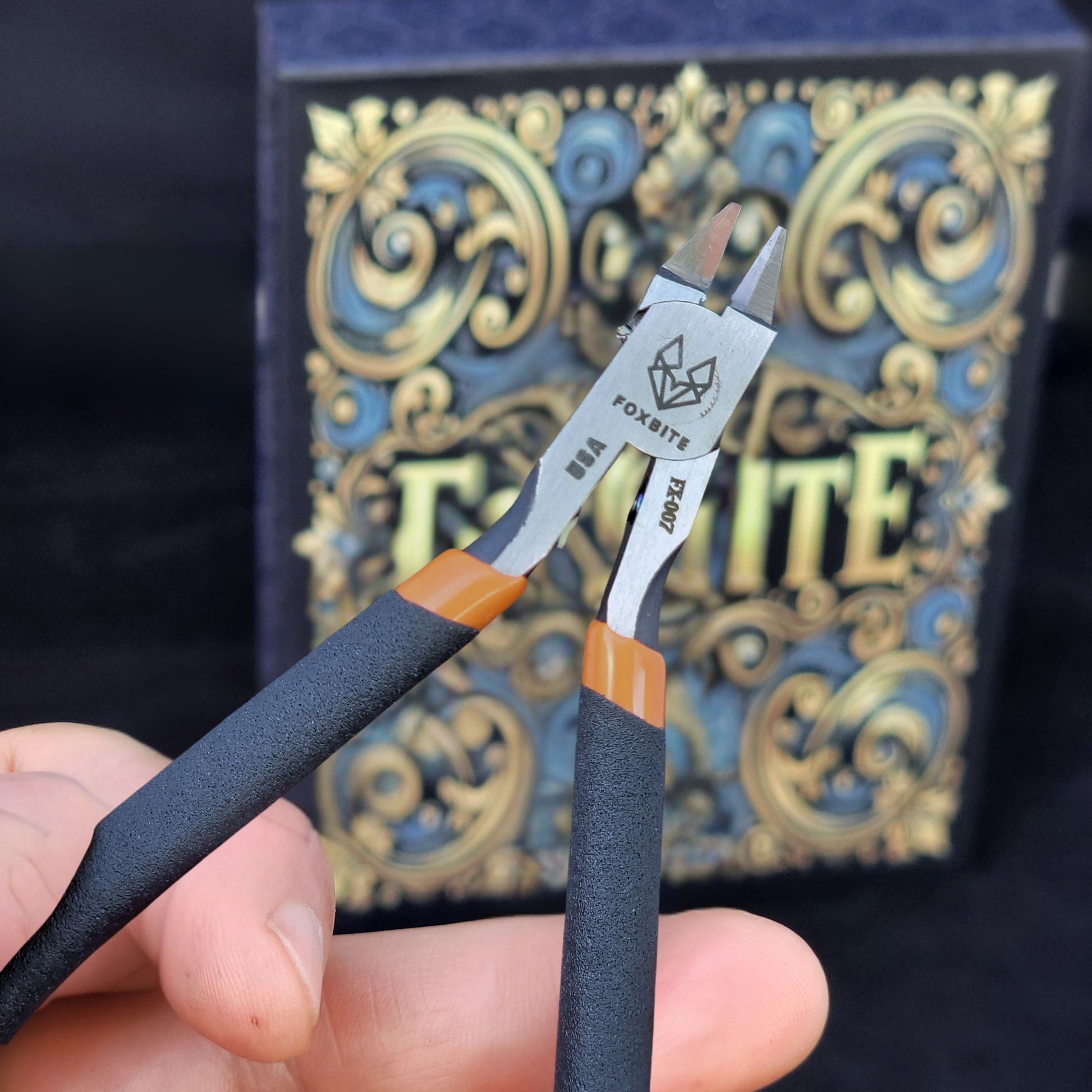 Pair of pliers held in hand with a decorative box in the background

